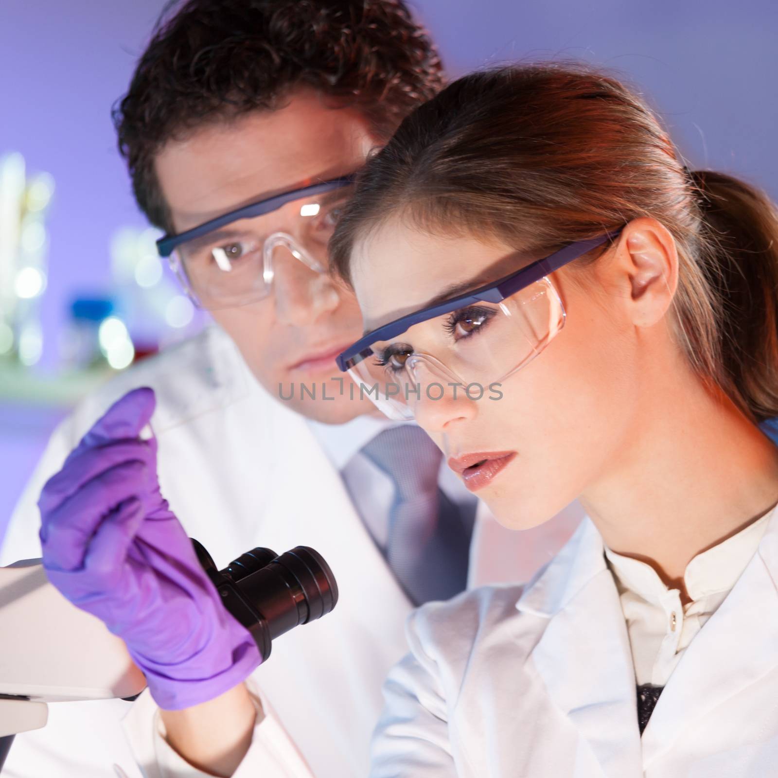 Attractive young scientist and her post doctoral supervisor looking at the microscope slide in the forensic laboratory.