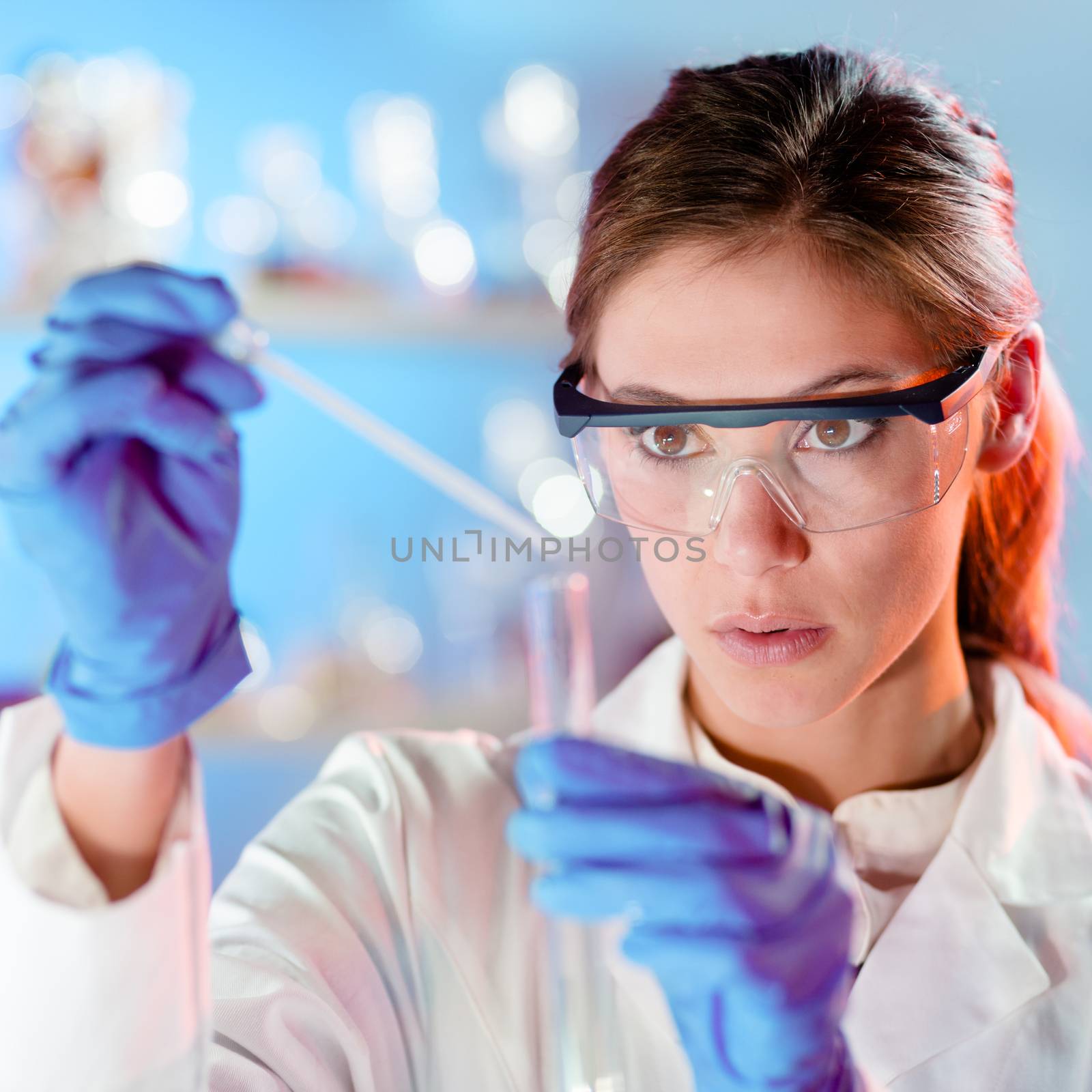 Focused young life science professional pipetting solution into the glass cuvette. Lens focus on the researcher's eye.