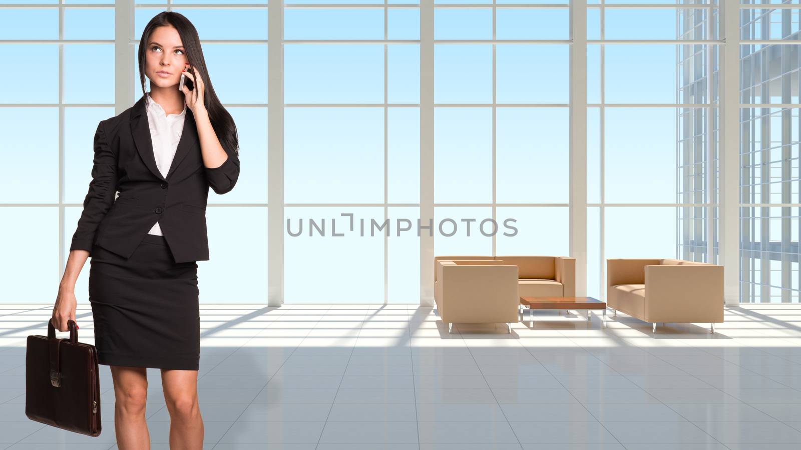 Businesswoman holding brifecase and using phone. Large window in office building as background
