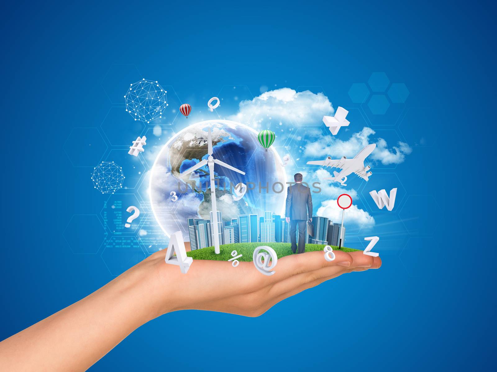 Hand holds city of skyscrapers on green grass and businessman walking forward. Earth and fying letters near hand. Element of this image furnished by NASA