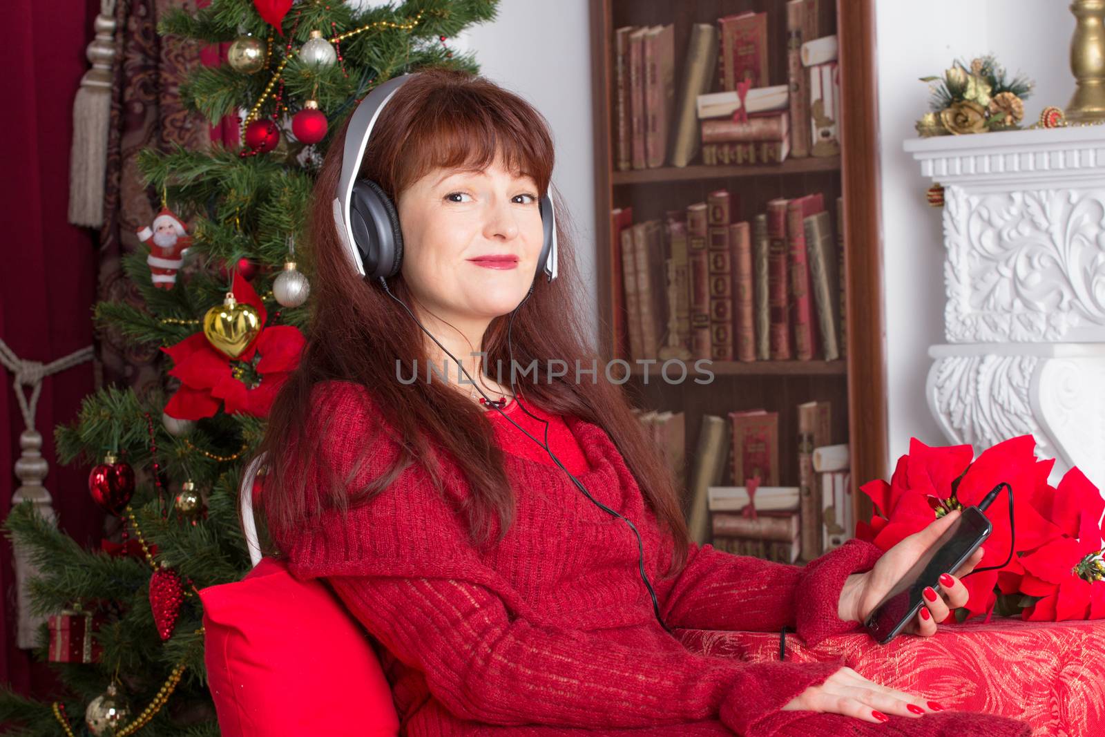 Beautiful adult woman listening music against Christmas tree