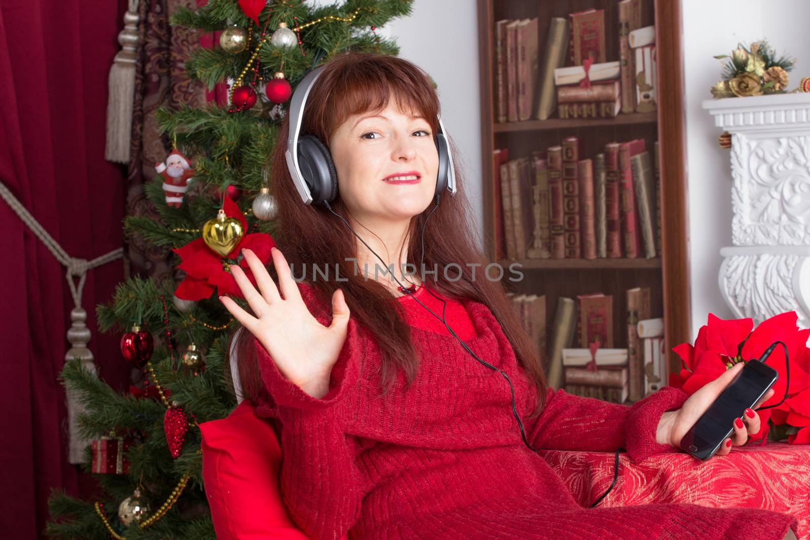 Beautiful adult woman listening music against Christmas tree