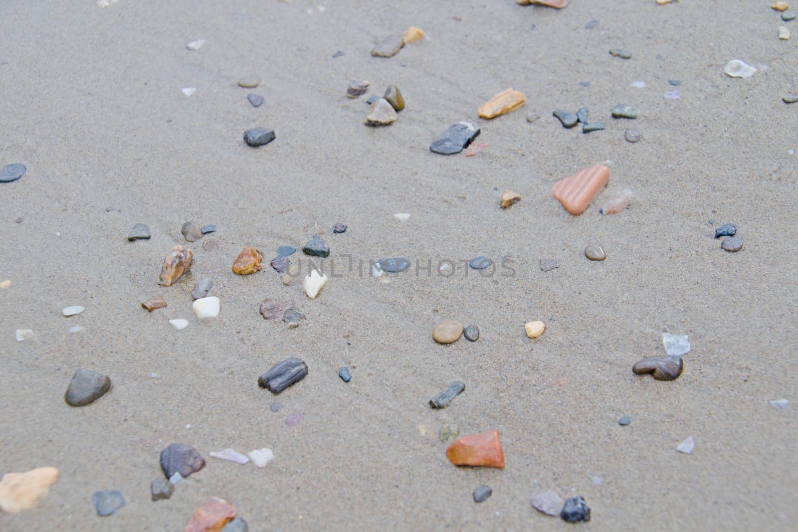 Photo shows a detail of the various stones on the sandy beach.