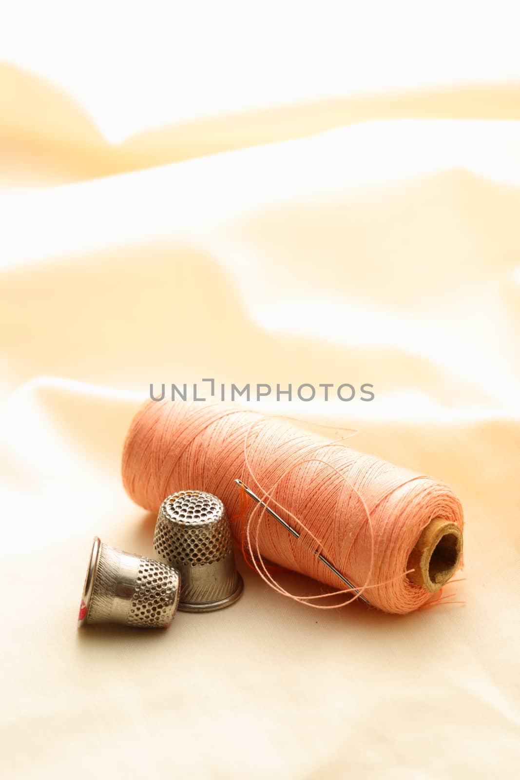 Sewing thimbles, bobbin and needle on silk cloth