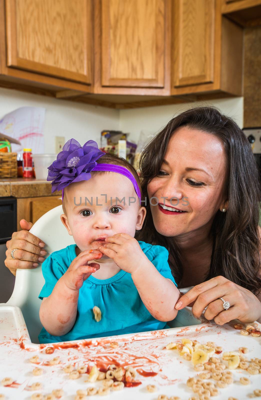 Mother in messy kitchen smiles as baby eats