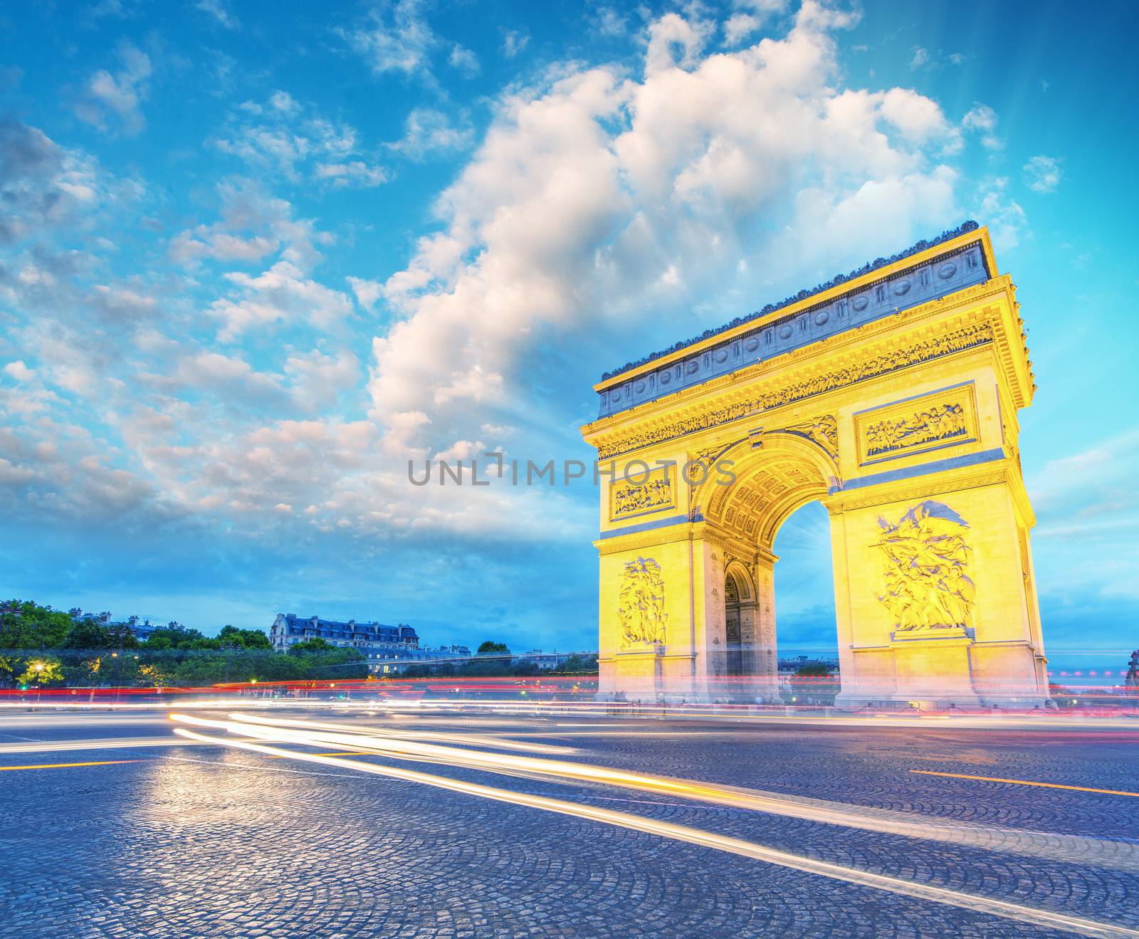Amazing sunset view of Triumph Arc in Paris with Etoile Roundabout traffic light trails.