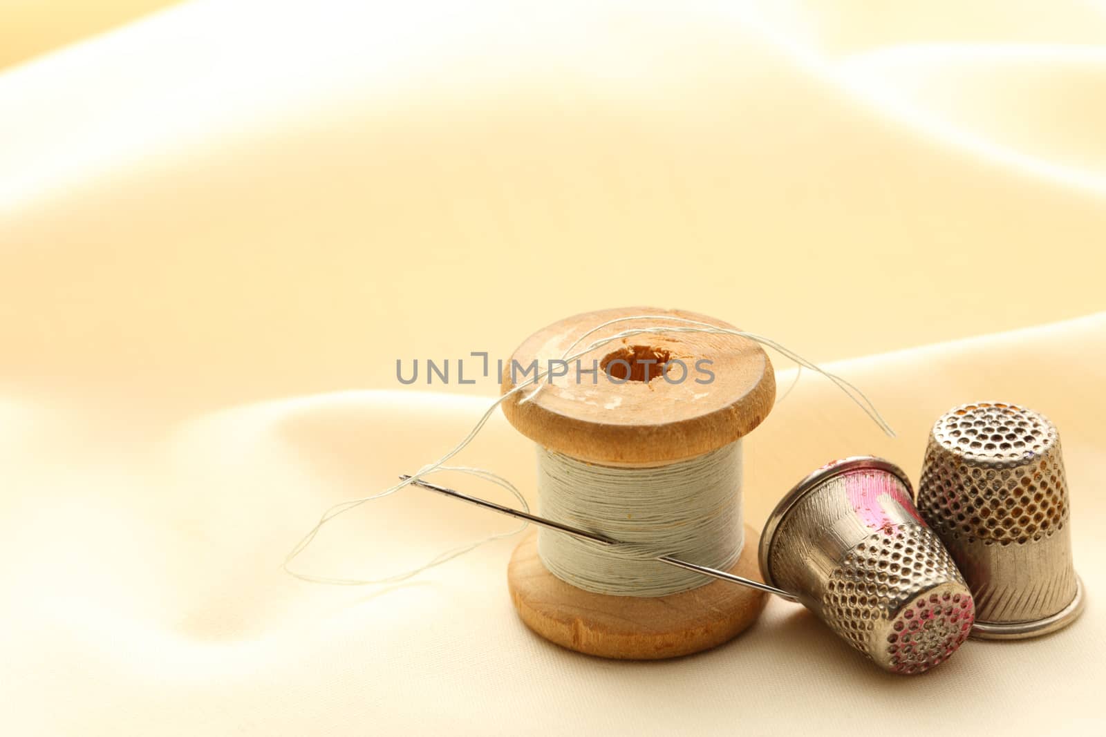 Sewing thimbles, bobbin and needle on silk cloth