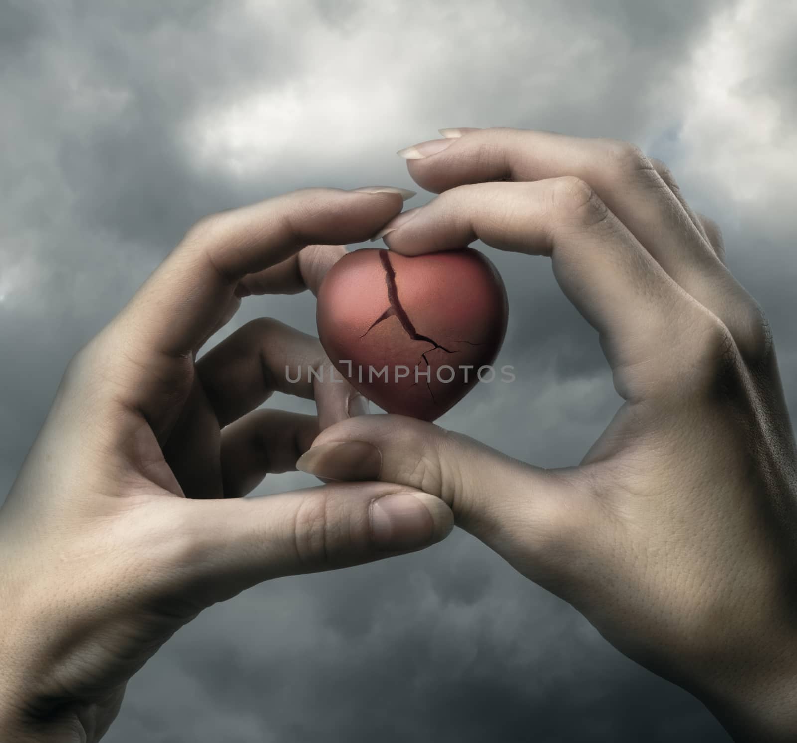 Broken red heart in hands on stormy sky