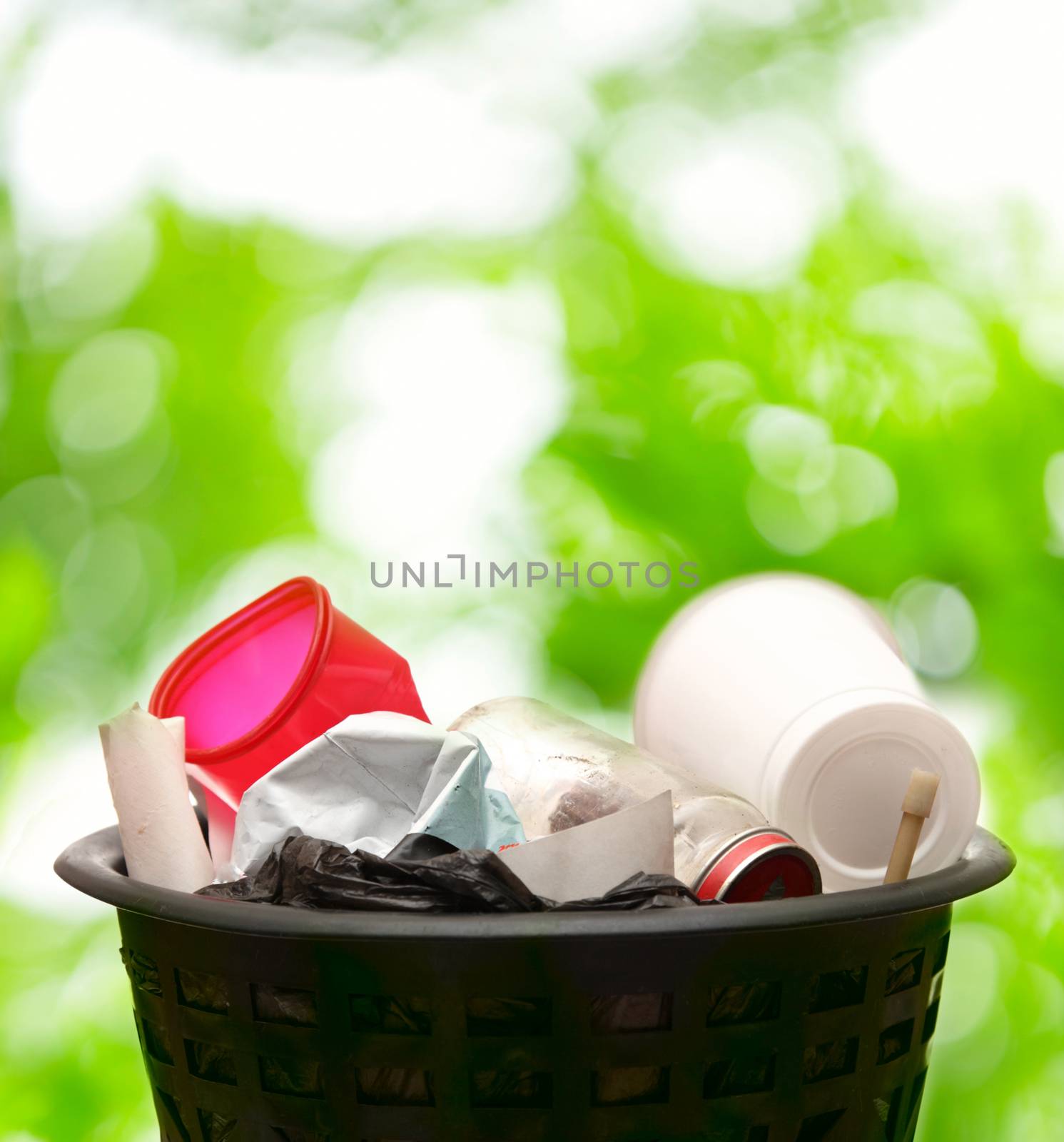 Full wastebasket on green leaves background