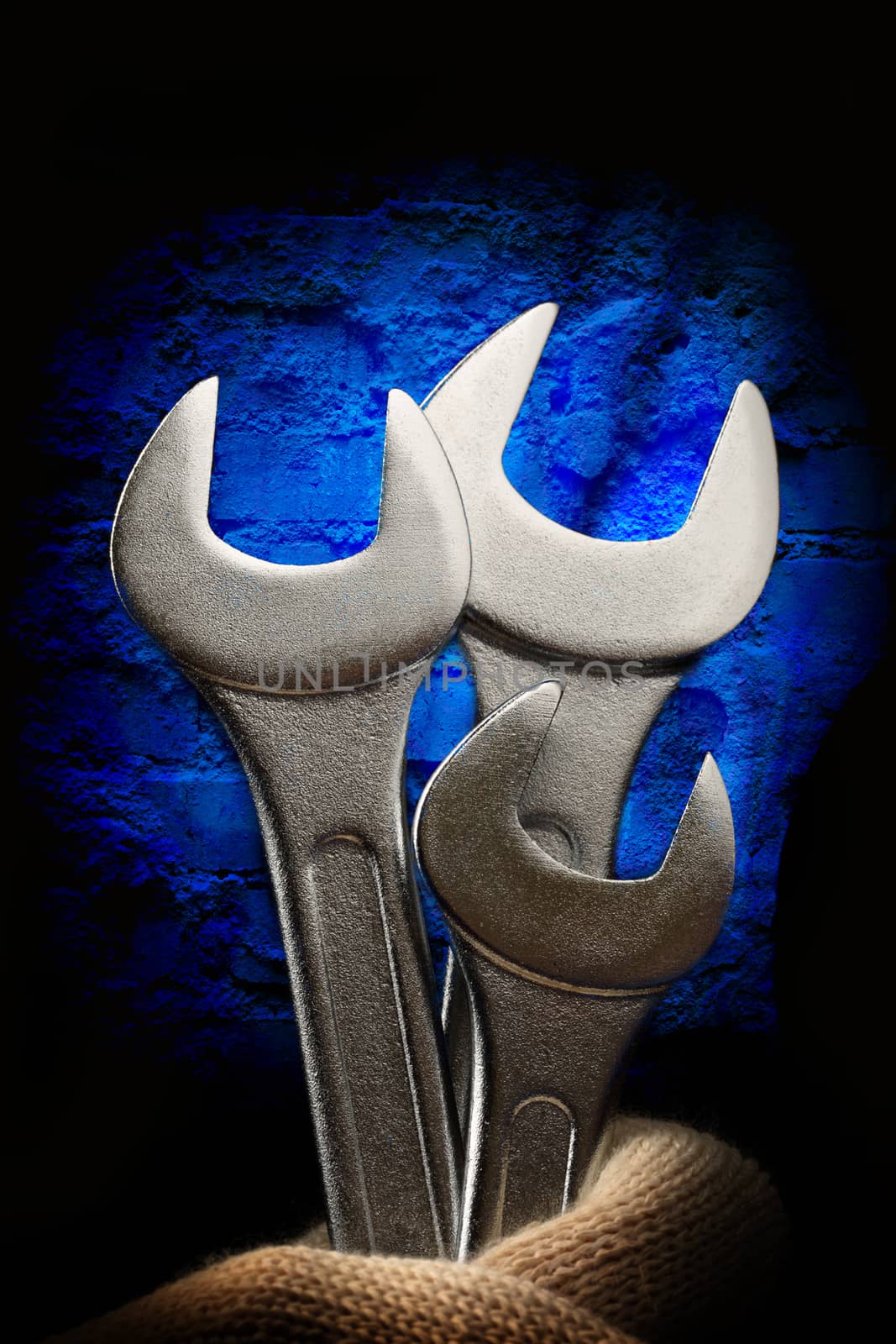 Metallic wrenches in male hand on wall background