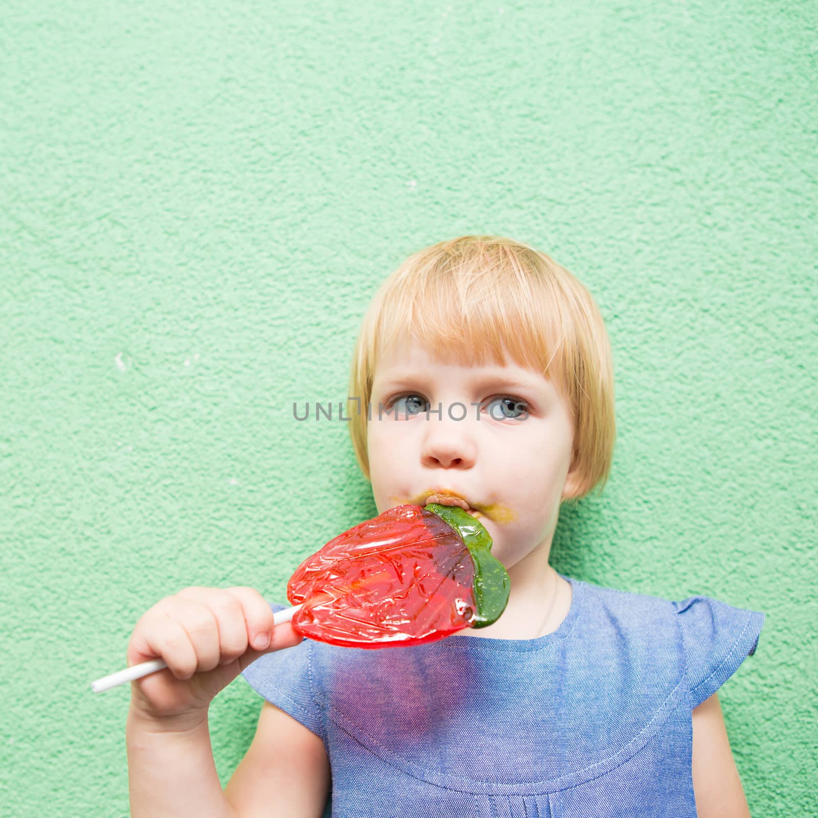 Beautiful little girl holding a big strawberry shaped lollipop