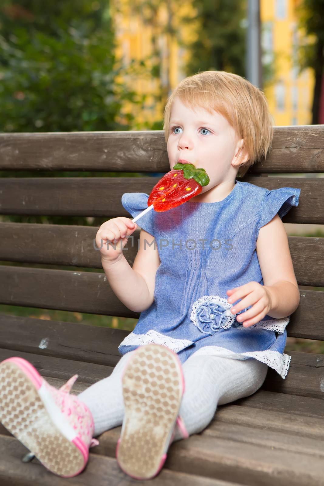 Beautiful little girl holding a big strawberry shaped lollipop