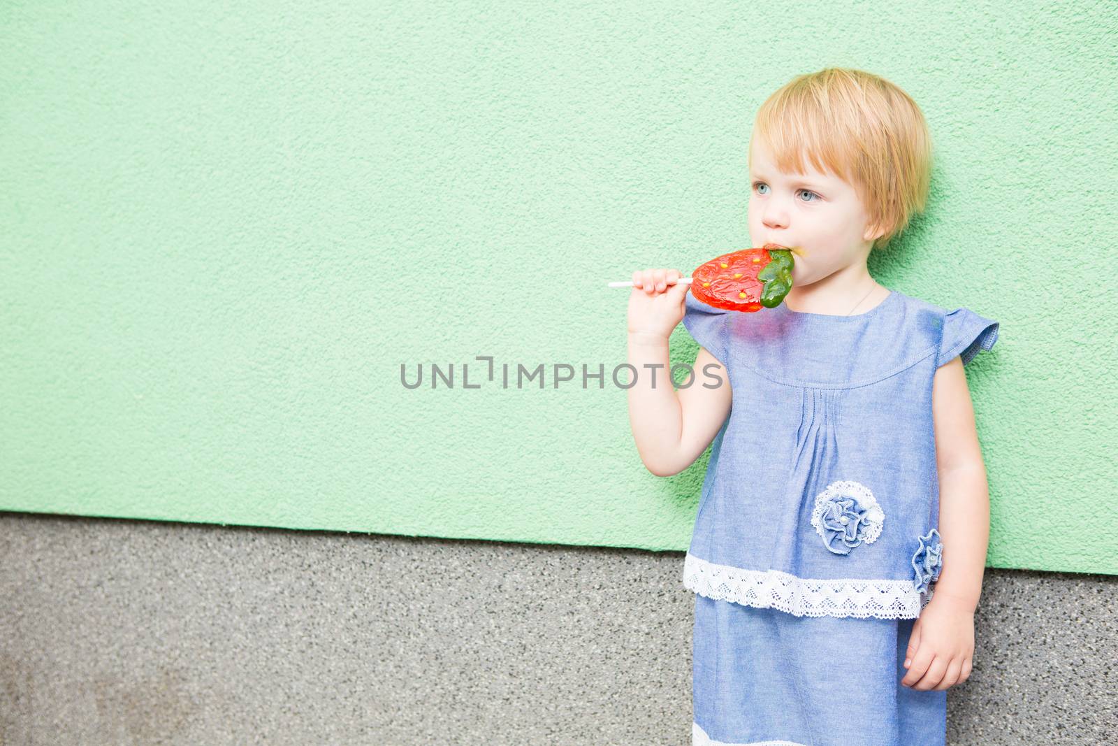 Beautiful little girl holding a big strawberry shaped lollipop