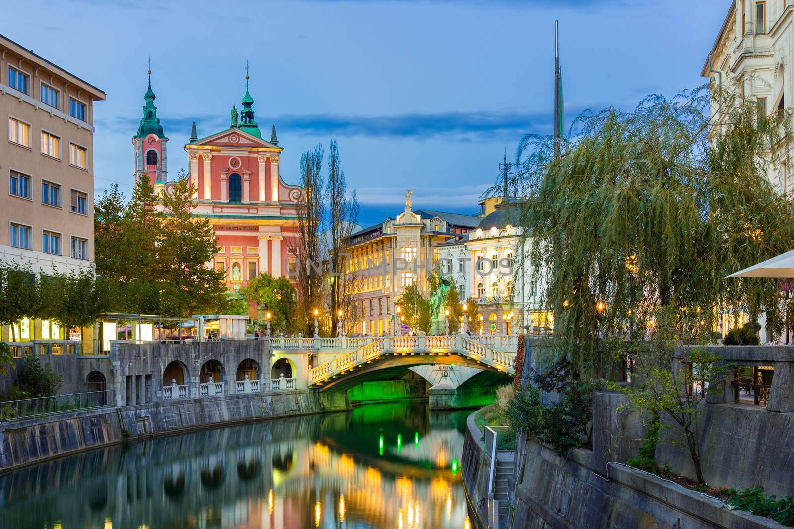 Romantic medieval Ljubljana's city center, capital of Slovenia, Europe. Night life on the banks of river Ljubljanica where many bars and restaurants take place. Franciscan Church in background