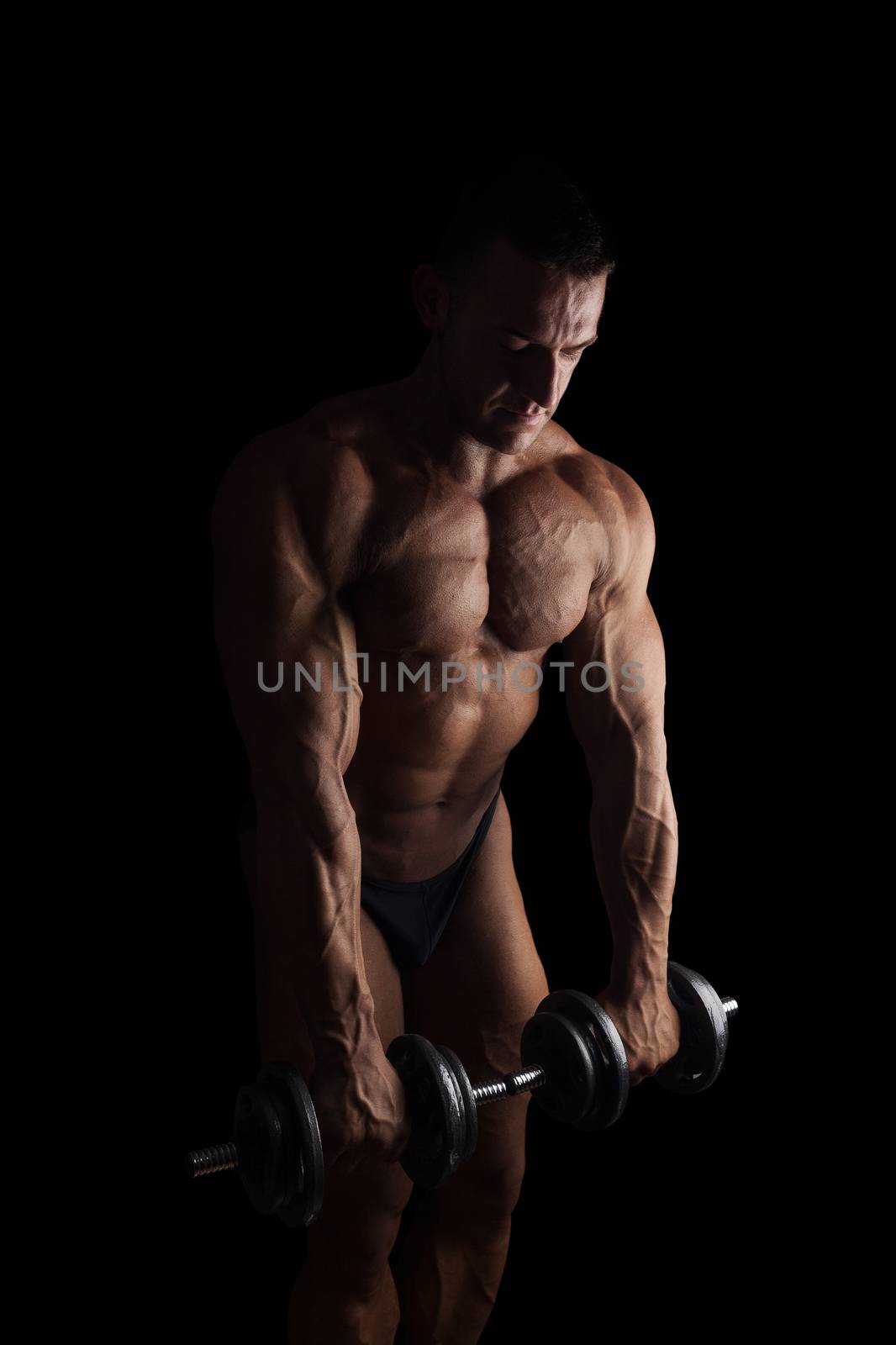 Sexy shirtless bodybuilder holding dumbbell isolated on black background. Extreme strength, muscles and fitness.