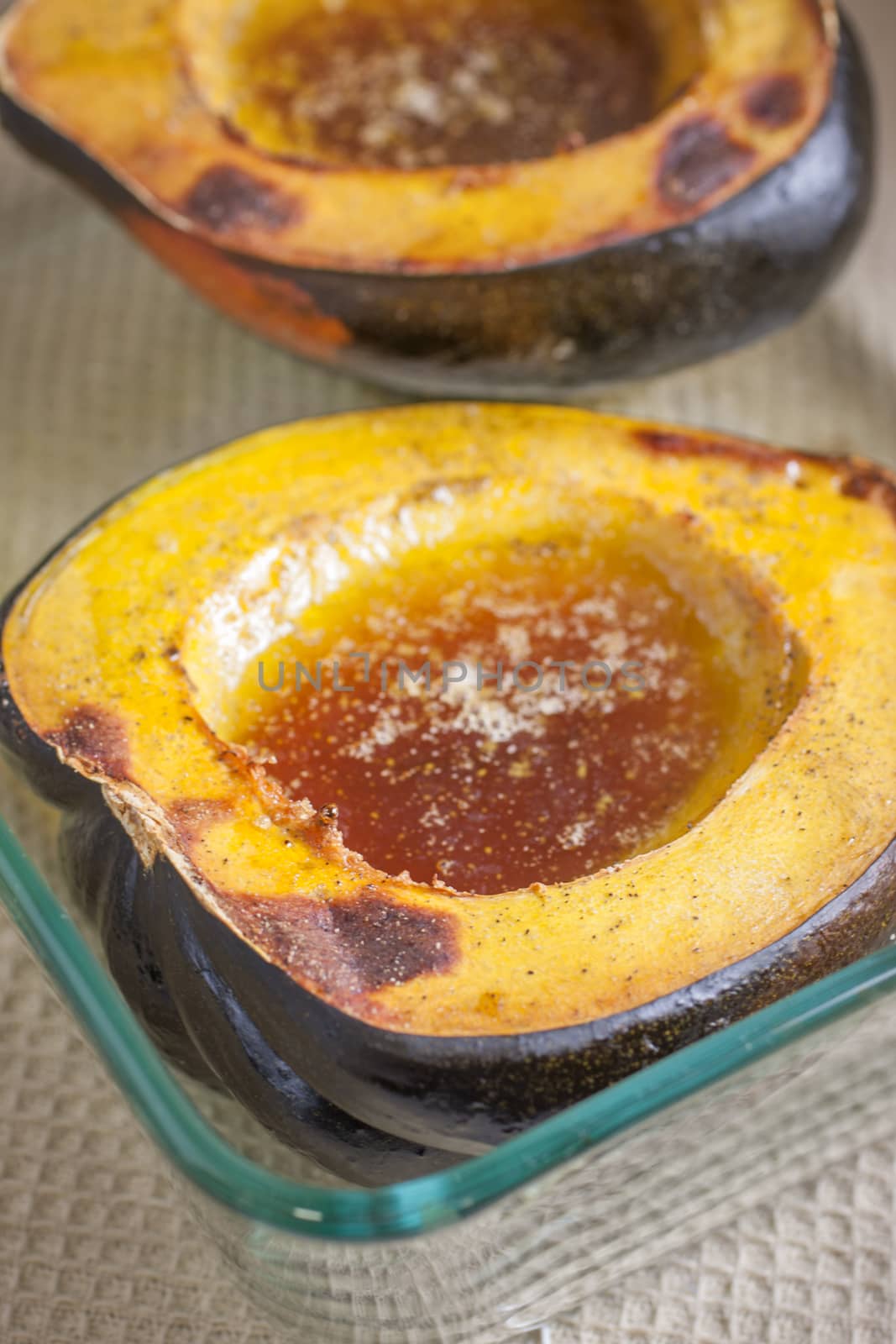baked acorn squash with butter, brown sugar, and maple syrup in a glass baking dish.