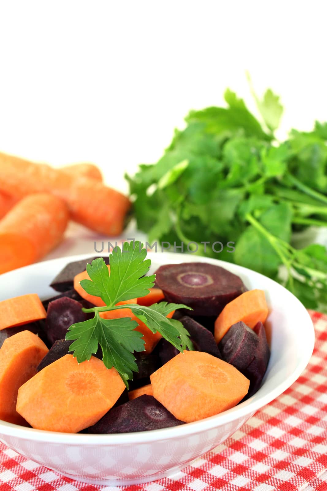 orange and purple carrots with green parsley on a light background