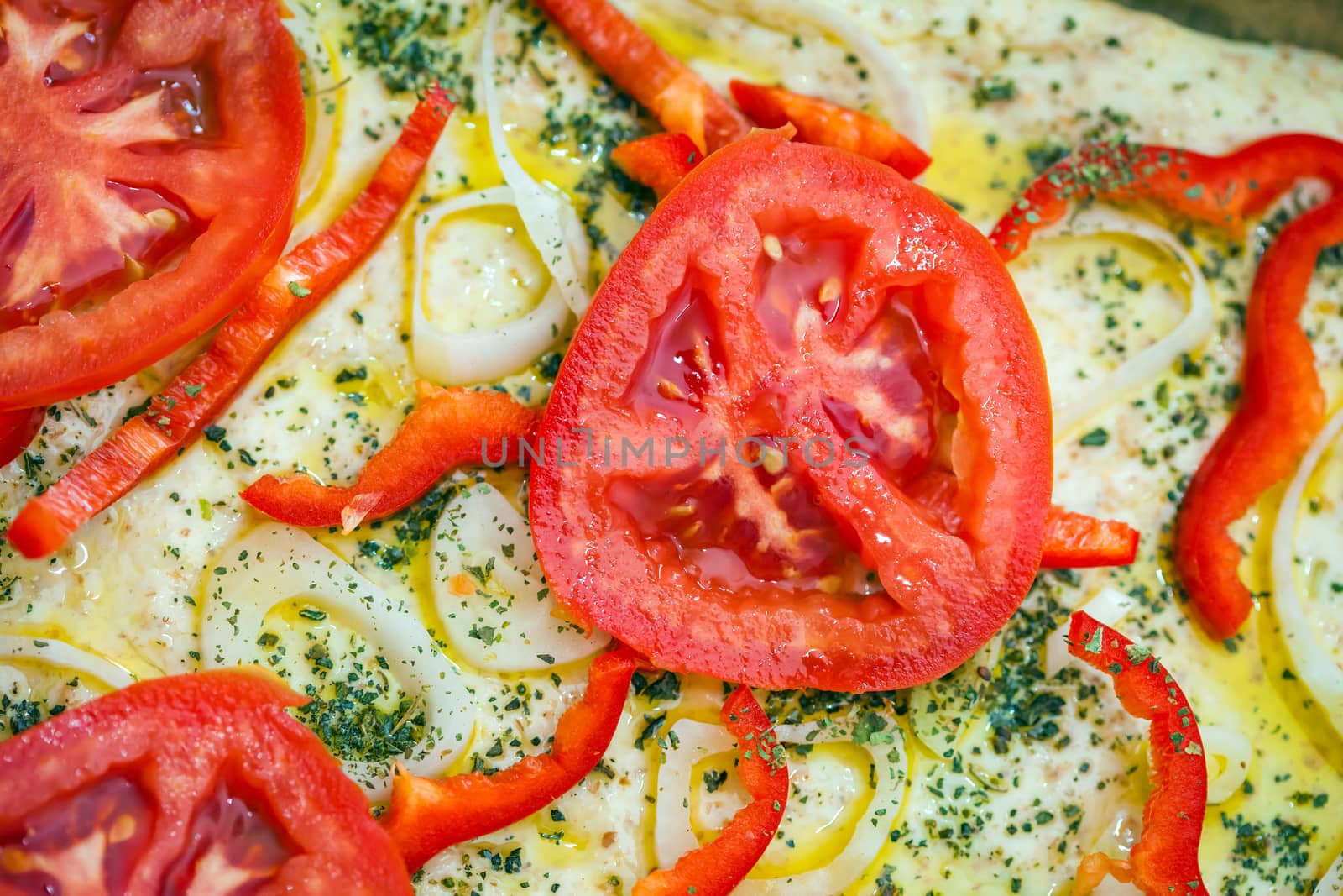 Tomato slice detail of traditional Italian focaccia bread with red peppers, onions, basil and olive oil on pan ready to cook