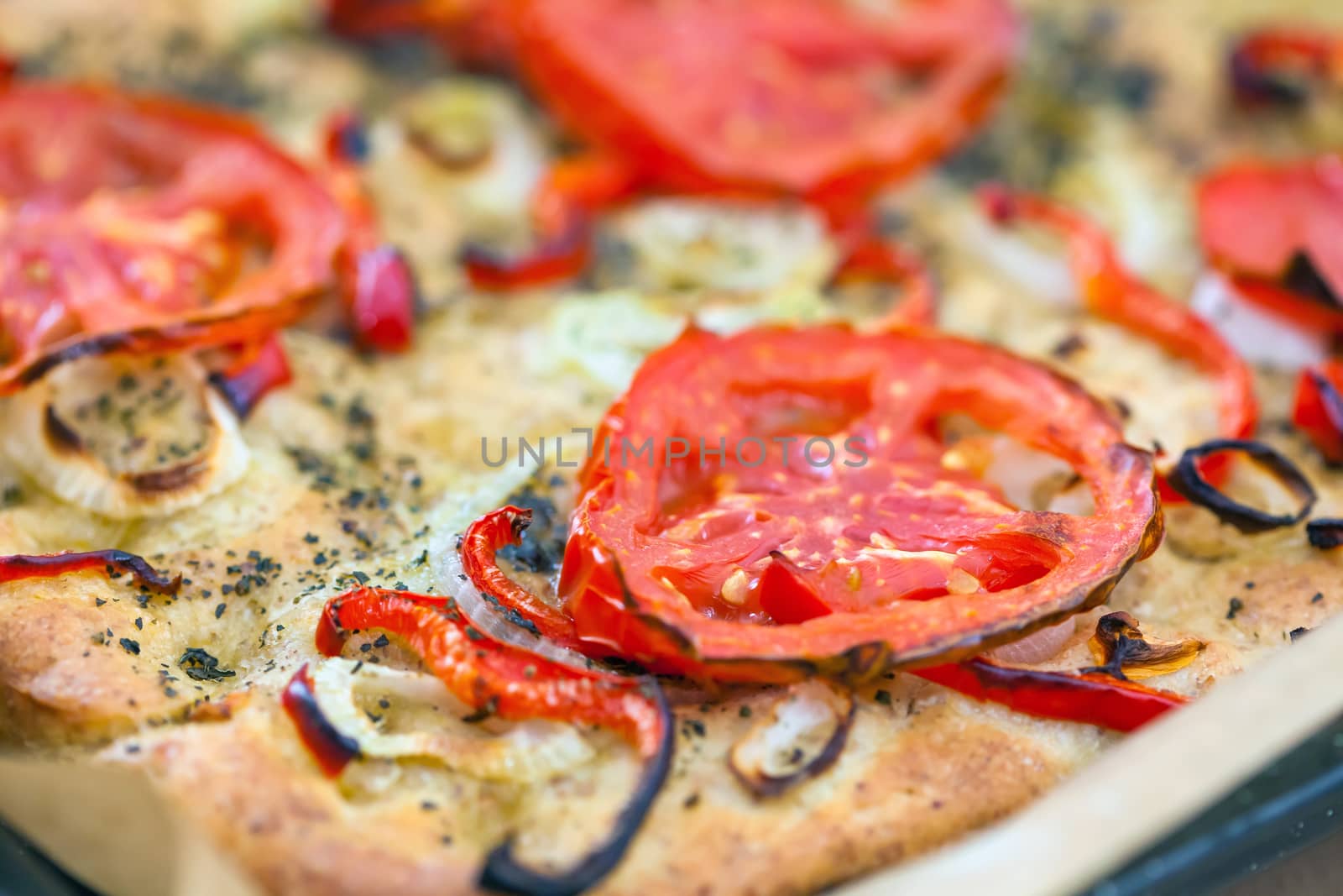 Delicious fresh traditional Italian focaccia bread with tomatoes, red peppers, onions, basil and olive oil on cooking pan