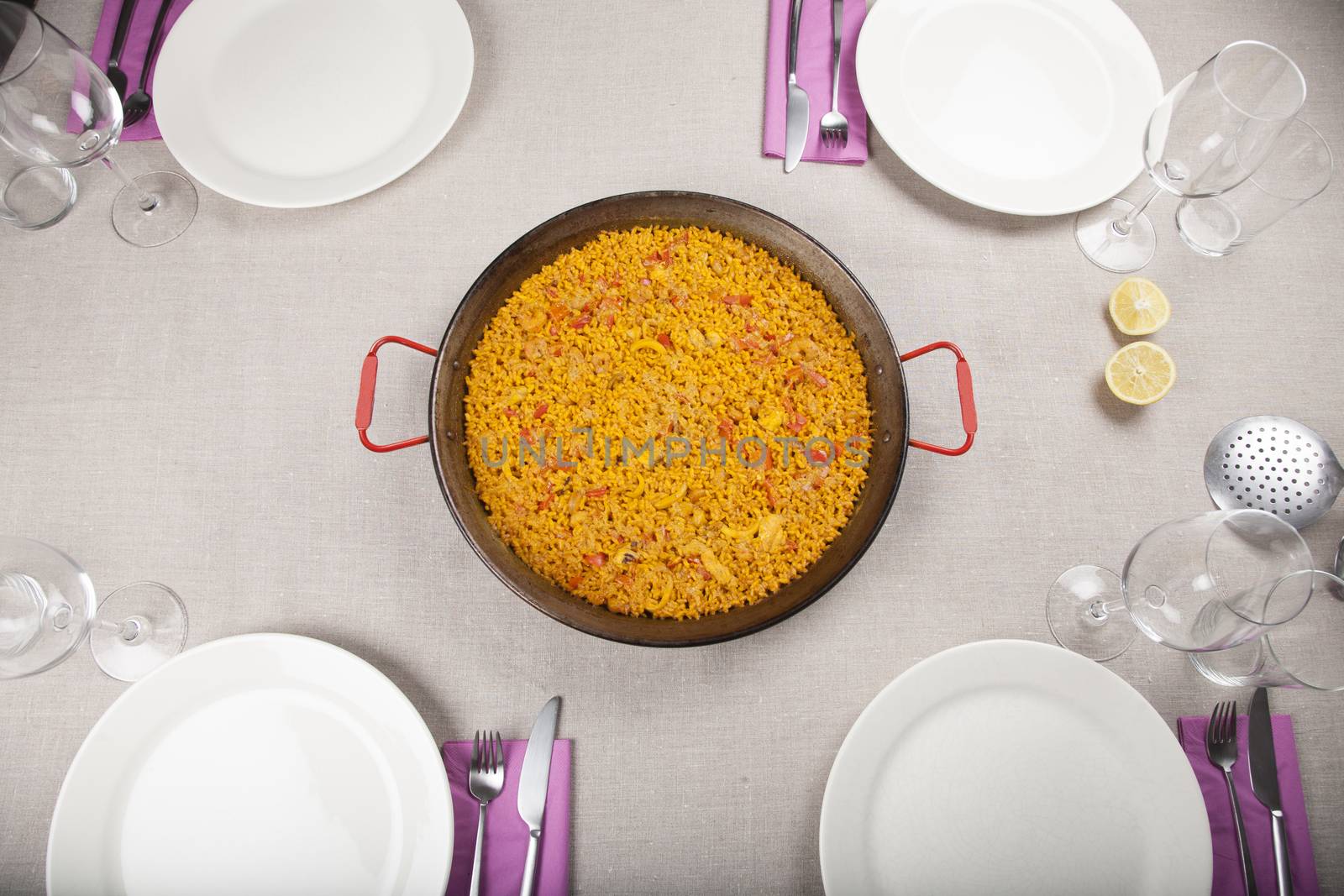 spanish paella in paellera pan on table with four dishes
