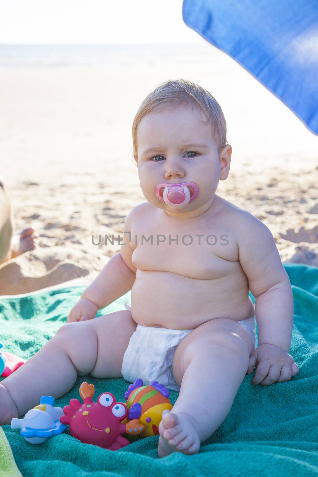 baby with white diaper on green towel at beach