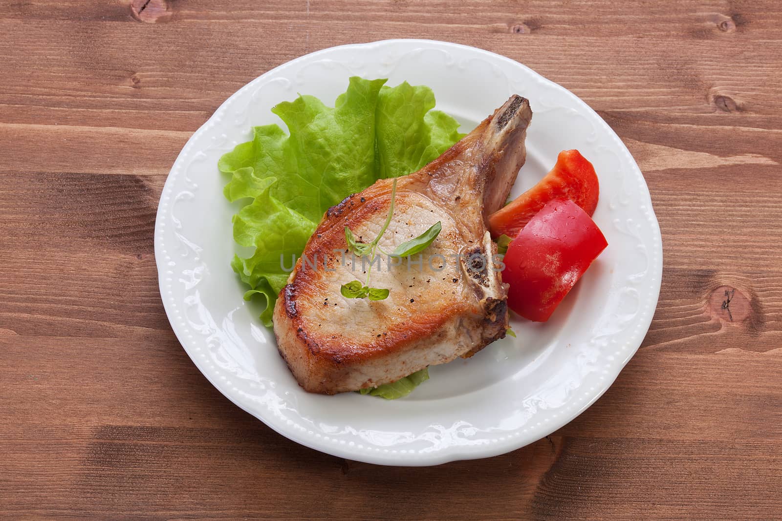 White plate with fried pork cutlet, lettuce and red sweet pepper on the wooden table