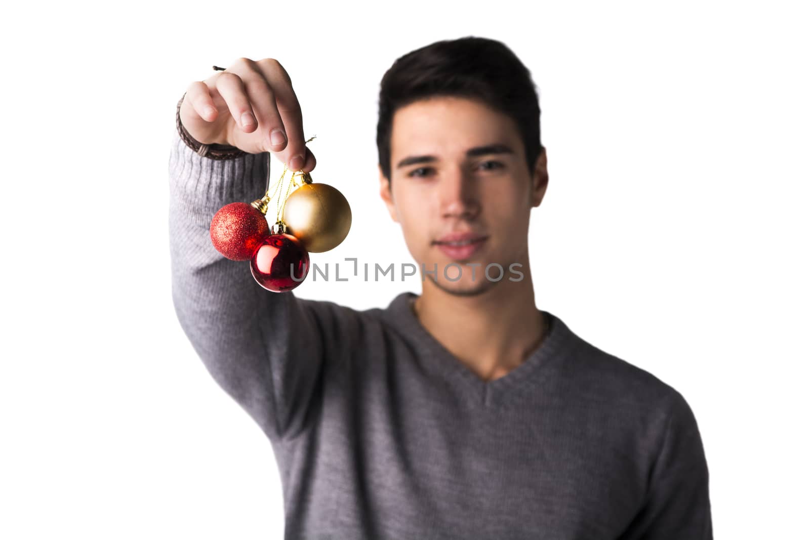 Handsome young man holding Christmas tree balls in front of his face, looking at camera on white background