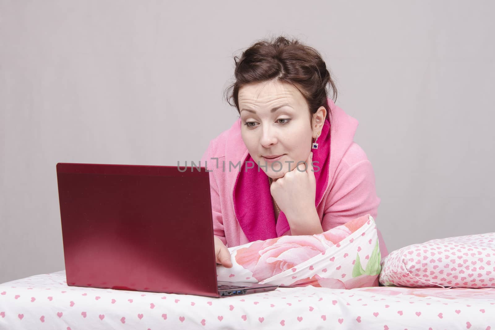 The girl lying in bed and works in the laptop