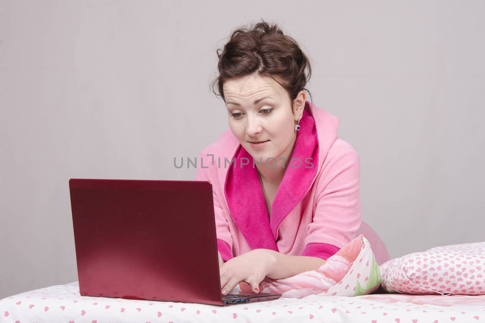 The girl lying in bed and works in the laptop