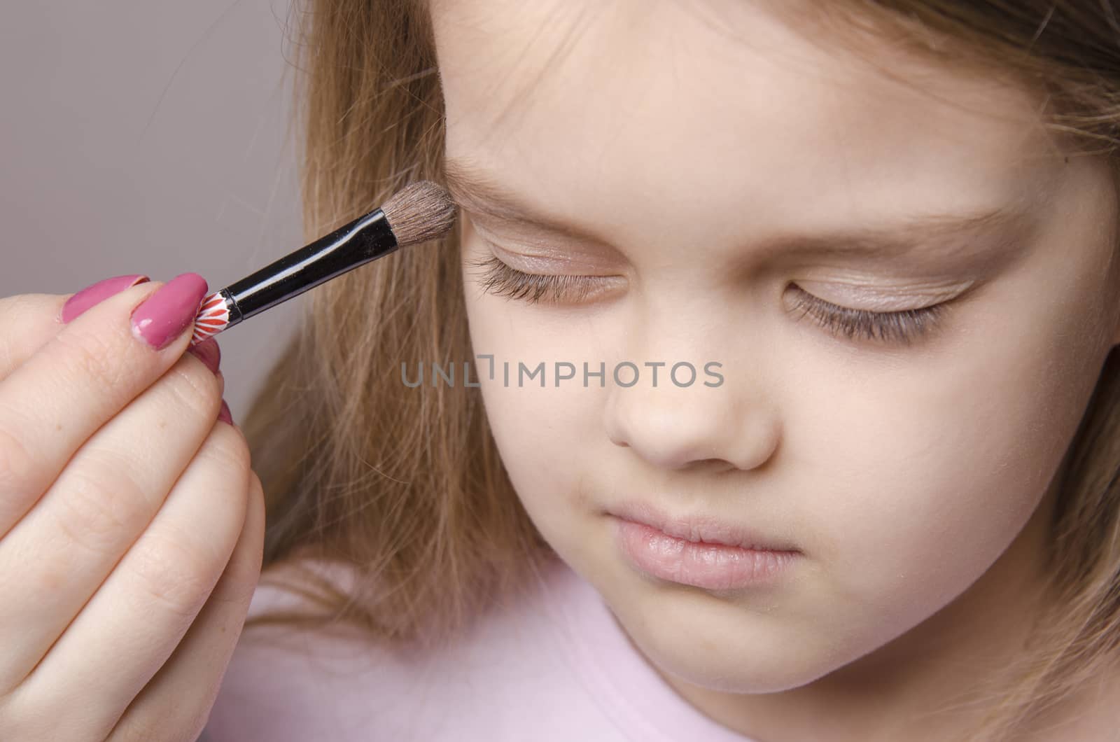 Makeup artist in the process of makeup colors eyelids on the face five year old girl