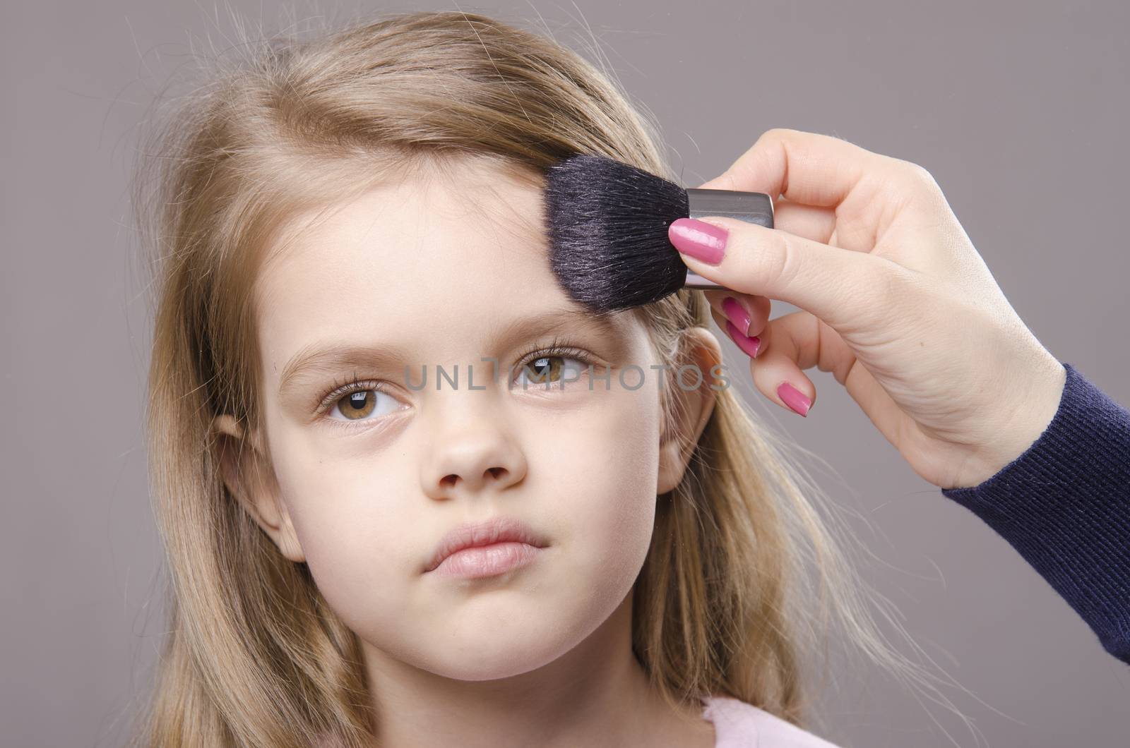 Makeup artist deals powder brush on the face of a five year old girl