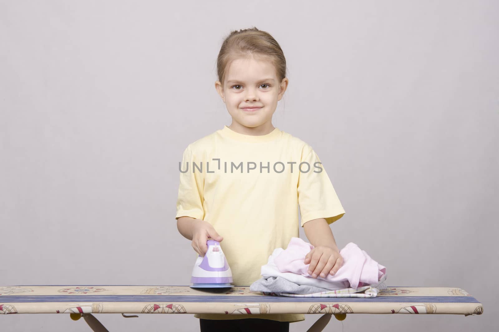 A five year old girl playing in a housewife, and stroking things iron