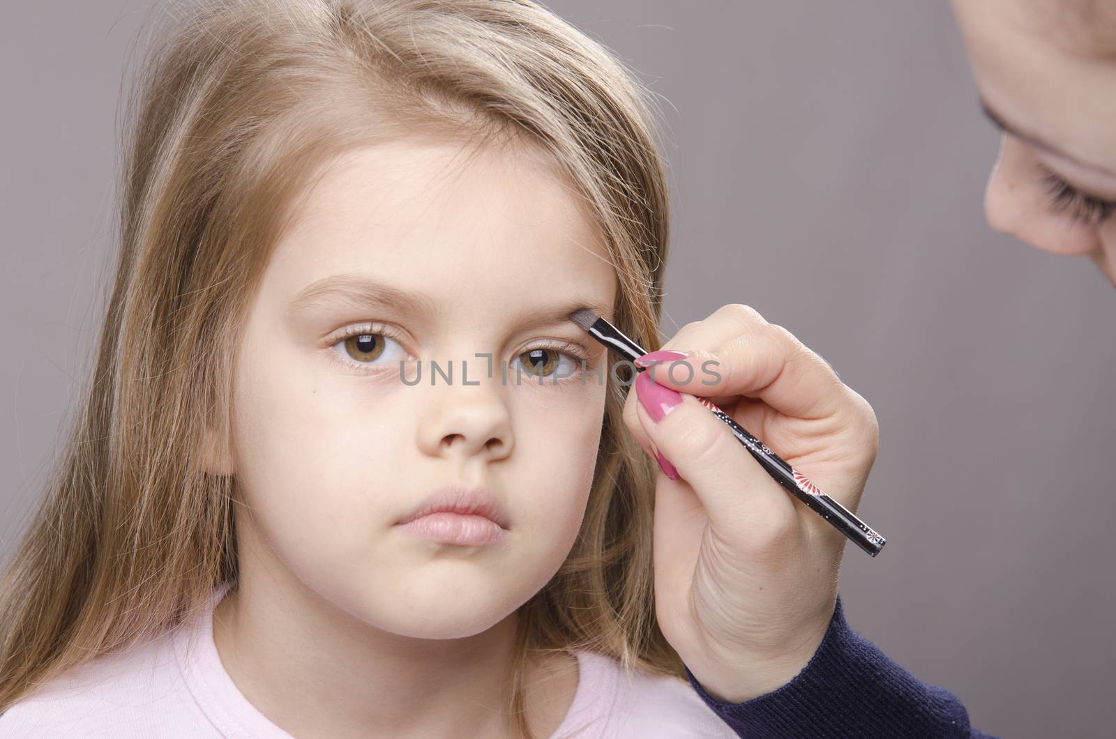 Makeup artist in the process of makeup brings eyebrows on the face five year old girl