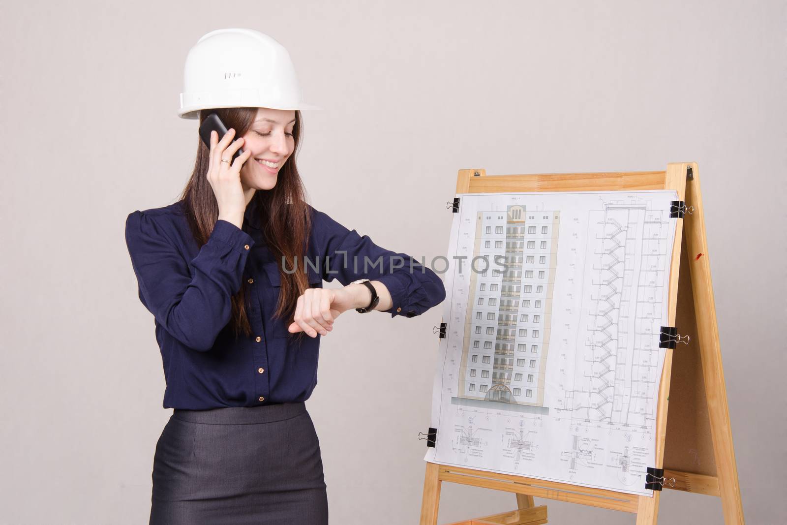 Young woman architect standing at drawing board mounted on the project of a multistory building