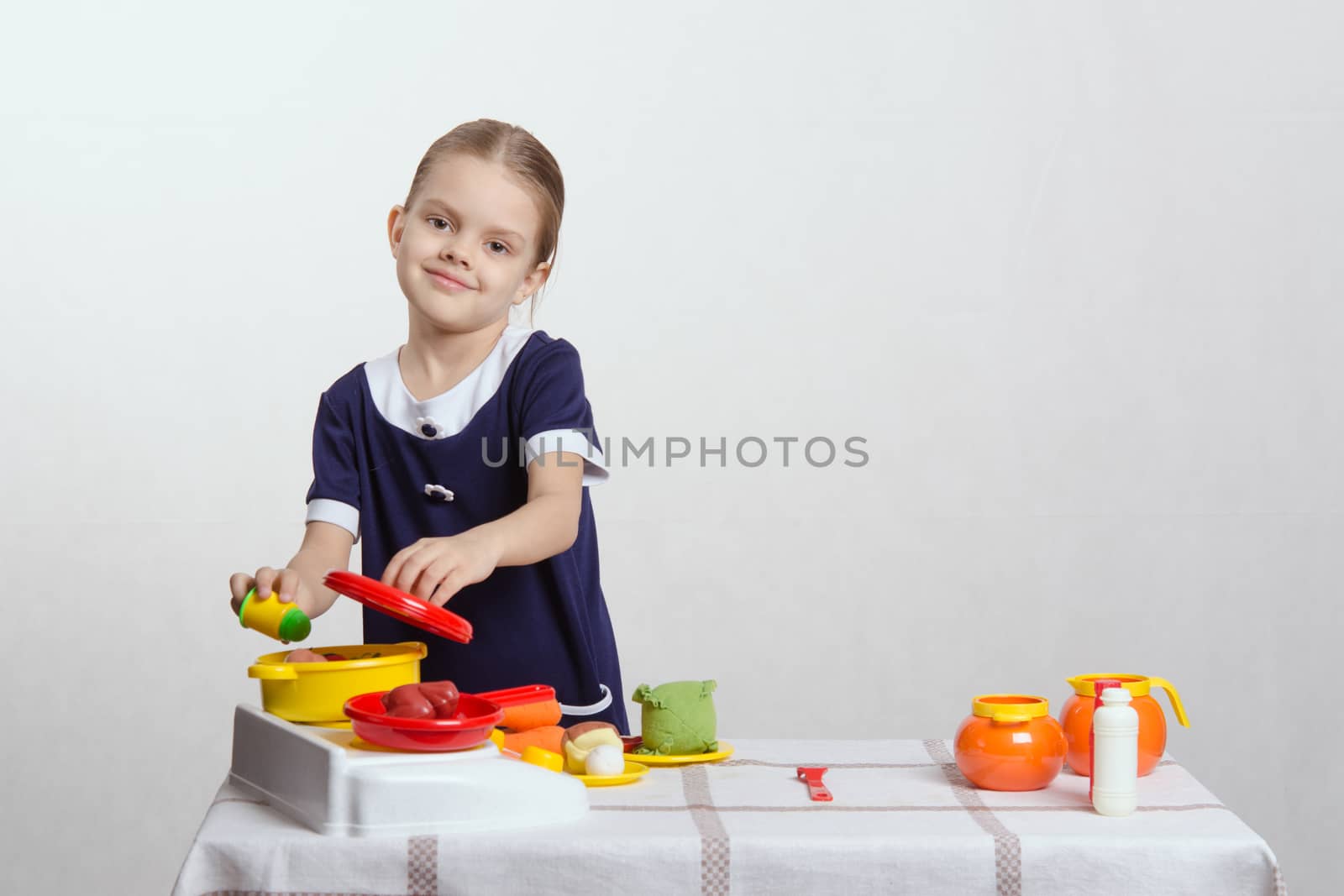 Five year old girl playing in a children's mistress dishes at a table covered with a cloth