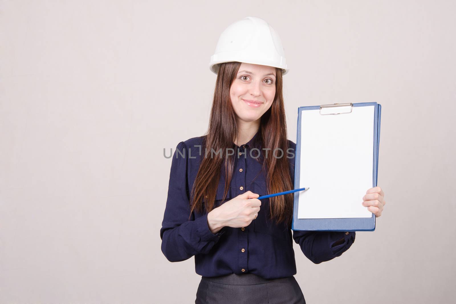 Young woman builder in helmet standing with a folder in hand