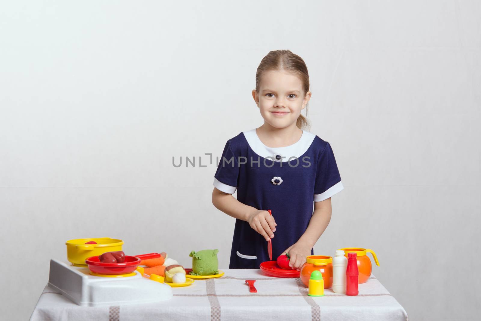 Five year old girl playing in a children's mistress dishes at a table covered with a cloth