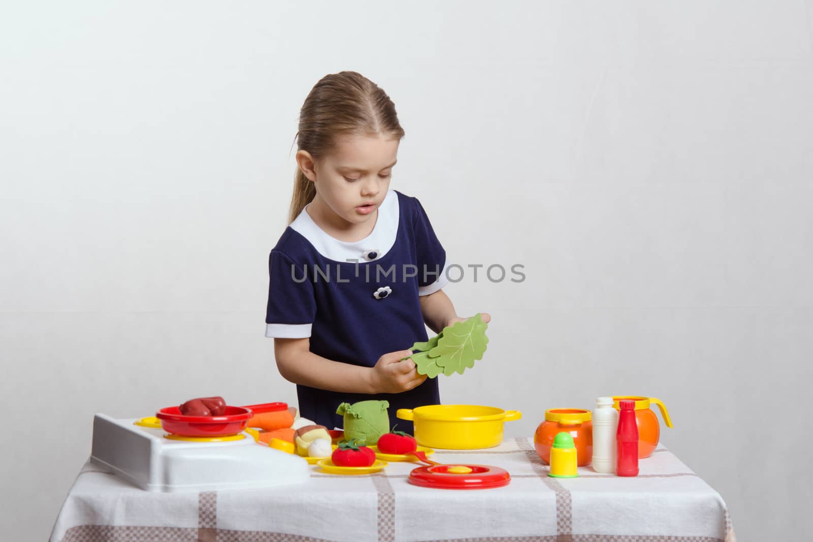 Five year old girl playing in a children's mistress dishes at a table covered with a cloth
