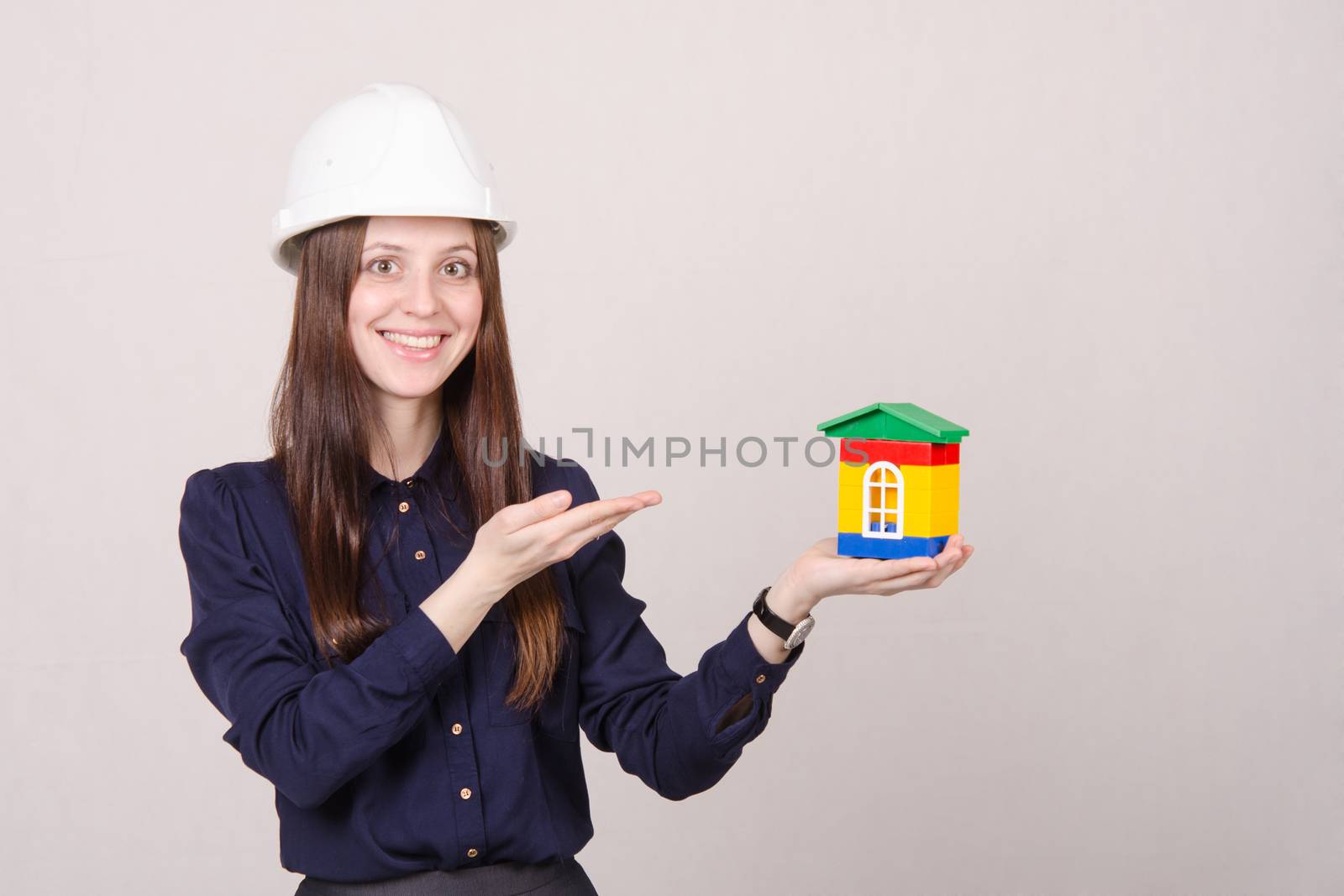 Young woman builder in helmet with a house worth in the hands of