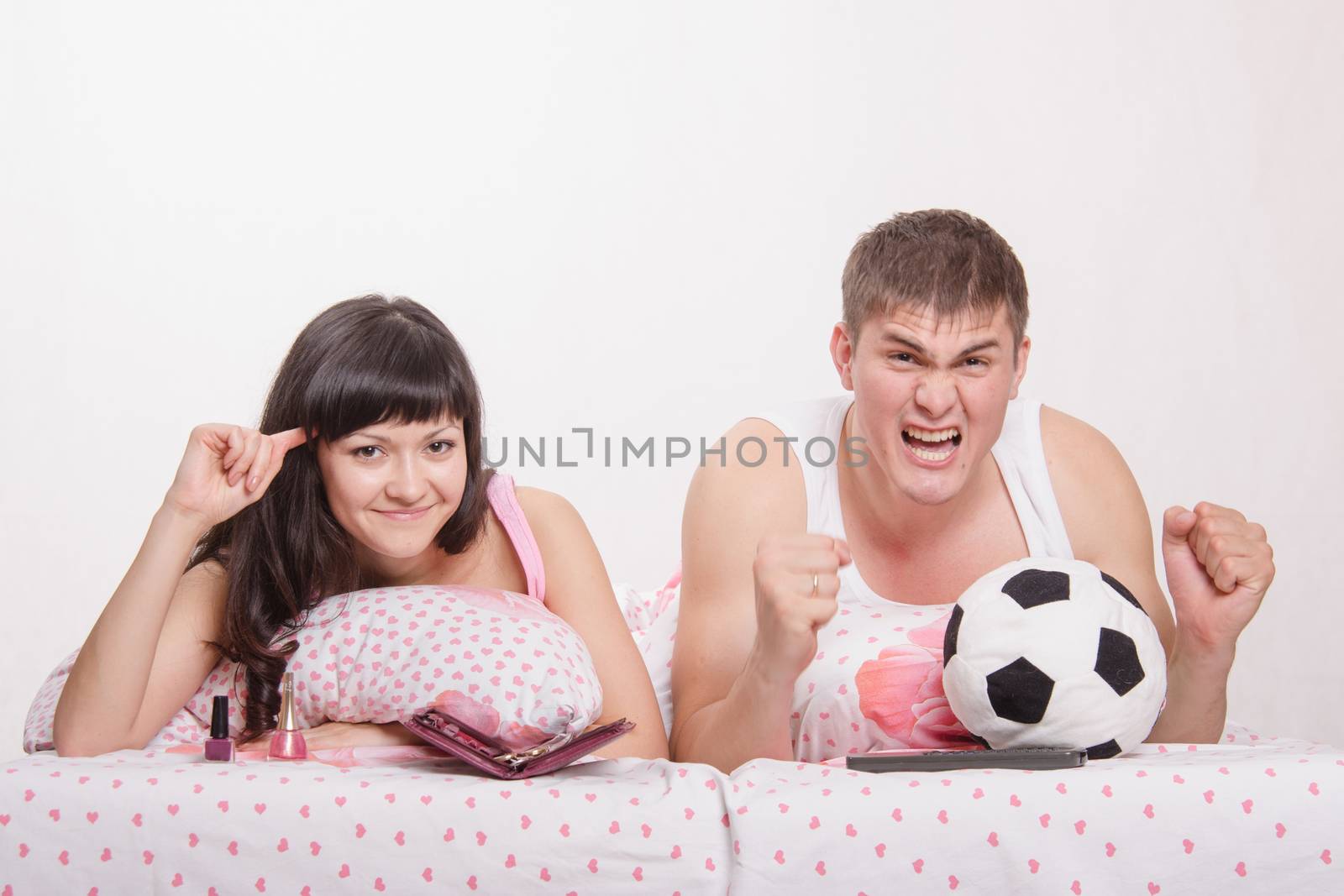 Young girl and a guy in bed. Beautiful girl has a manicure, man watches football on TV.