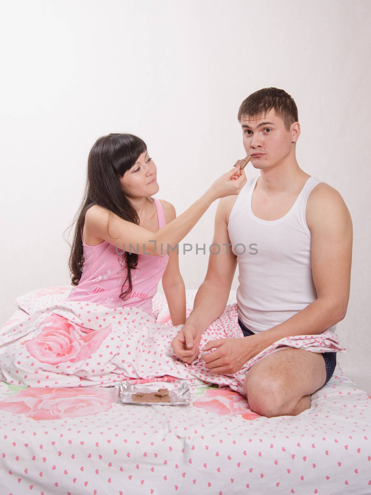 Young beautiful girl and the guy eat chocolate in bed