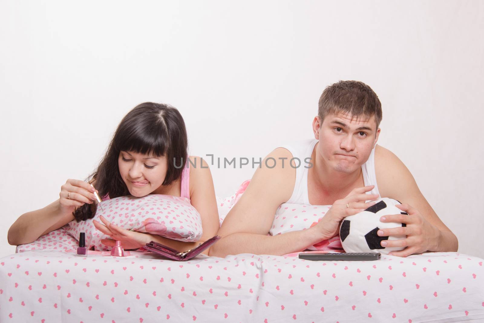 Young girl and a guy in bed. Beautiful girl has a manicure, man watching soccer on TV