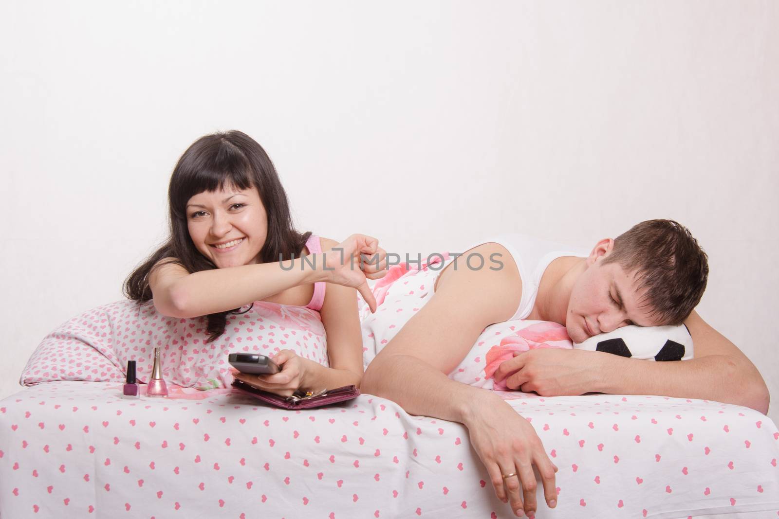 Young girl and a guy in bed. Beautiful girl has manicured nails on the hand, the guy watching soccer on TV