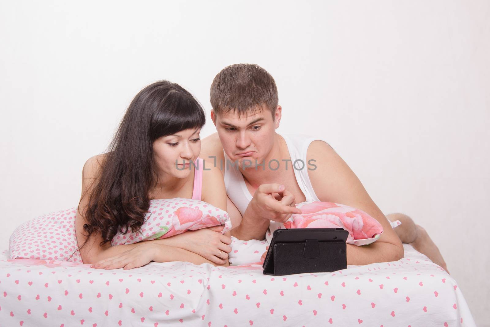Young beautiful couple watching a movie in the tablet computer while lying in bed