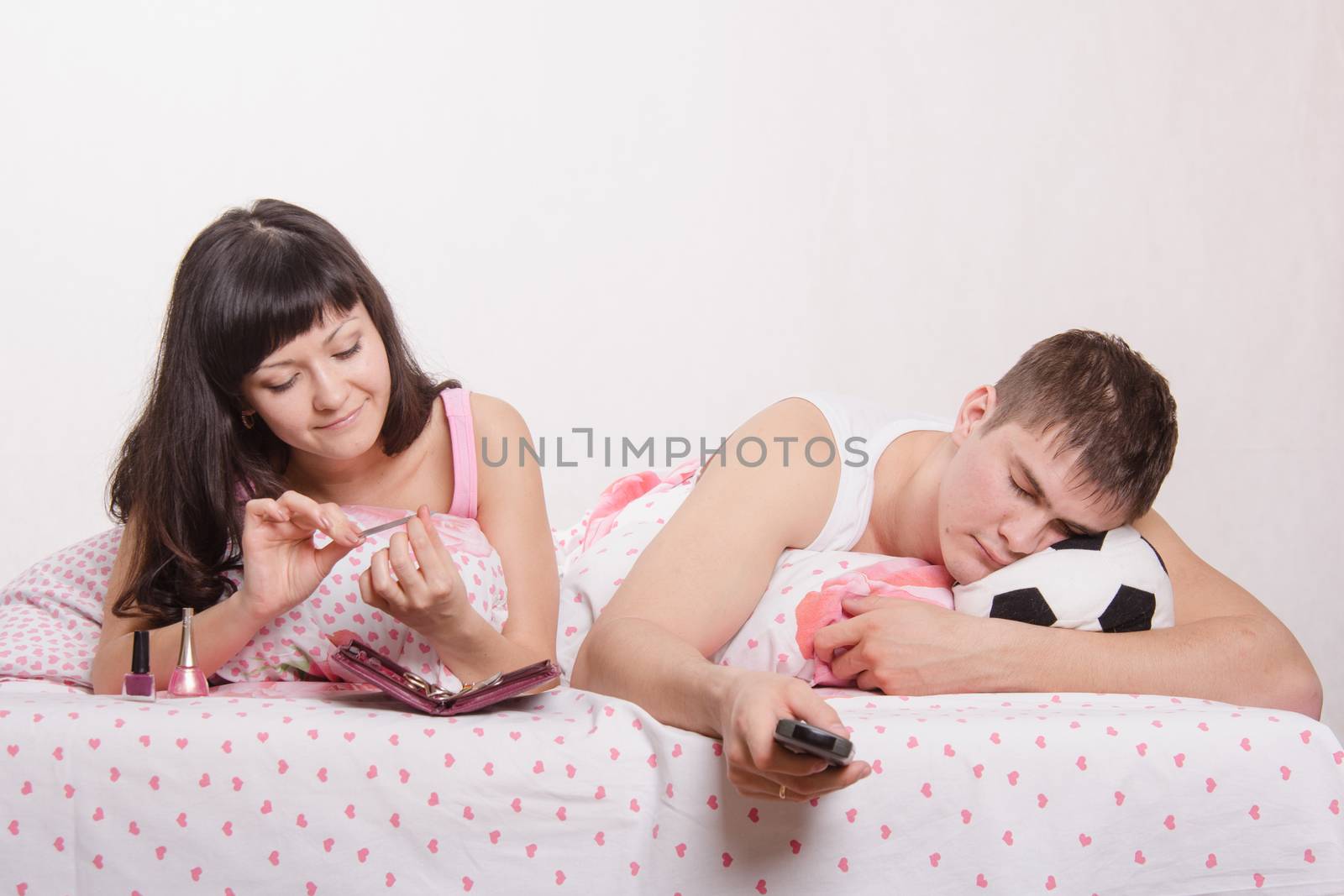 Young girl and a guy in bed. Beautiful girl has a manicure, man watching soccer on TV