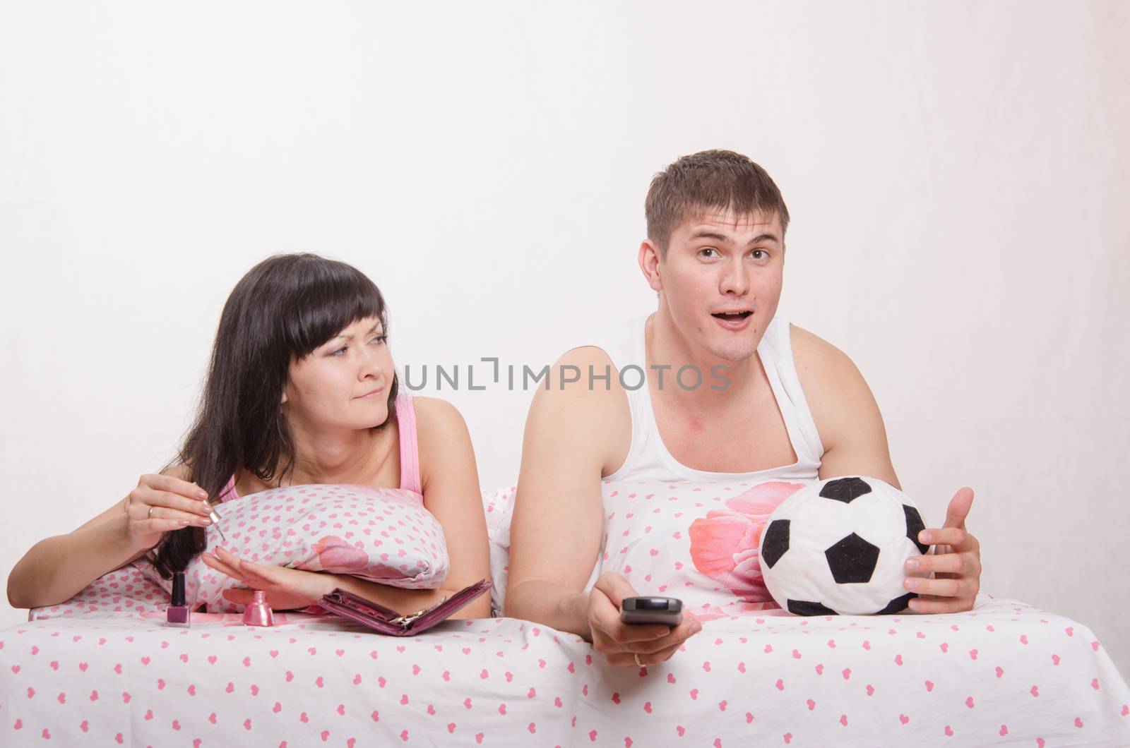 Young girl and a guy in bed. Beautiful girl has a manicure, man watching soccer on TV