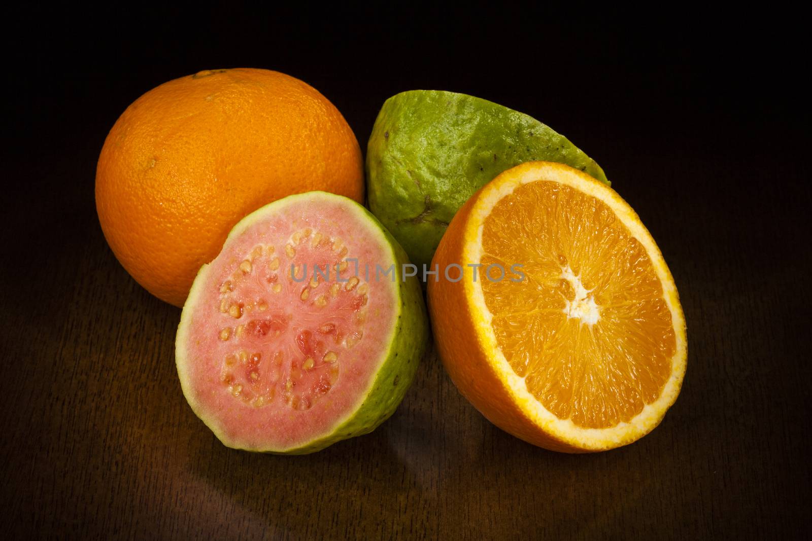 orange and guava cut in half over a table. Dark Background