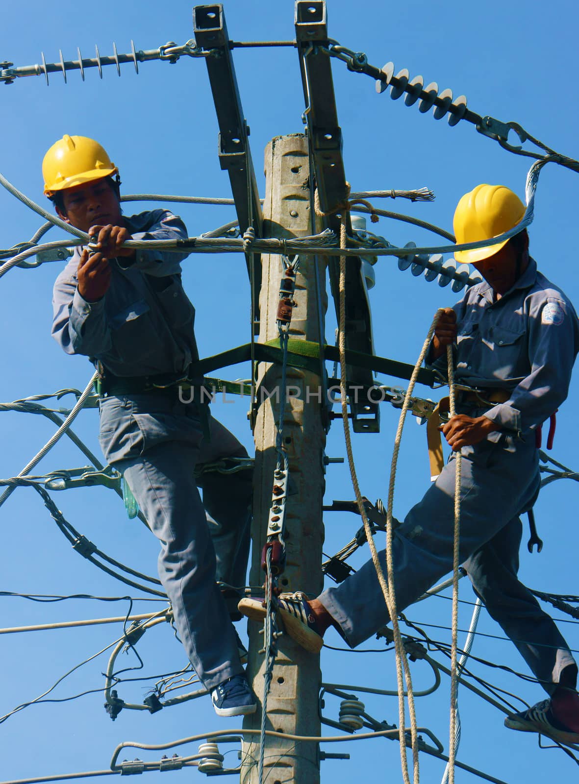 DONG THAP, VIET NAM- SEPT 23: Two Asian electrician climb high in pole to work, lineman with cable network, man repair electric post with belt safety, this is industry service, Vietnam, Sept 23, 2014