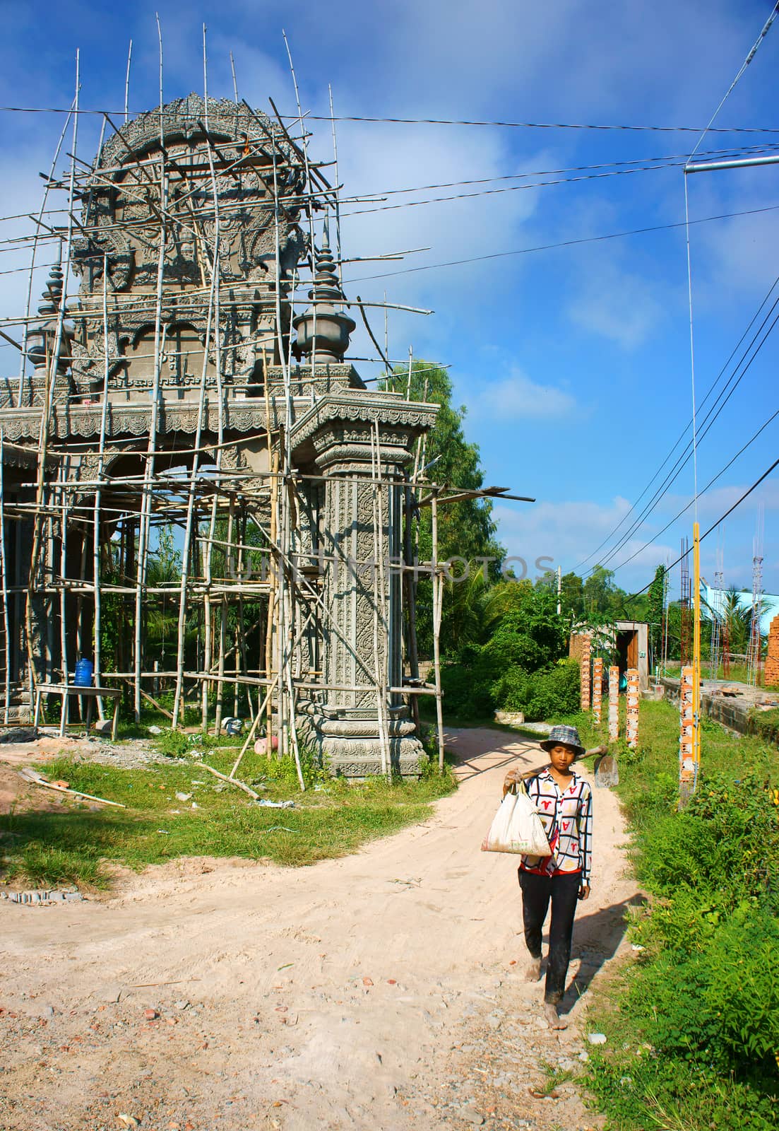 AN GIANG, VIET NAM- SEPT 20: Asian farmer carry tool walking on countryside path, construction work to construct khmer pagoda gate with pattern, development of religion, Vietnam, Sept 20, 2014
