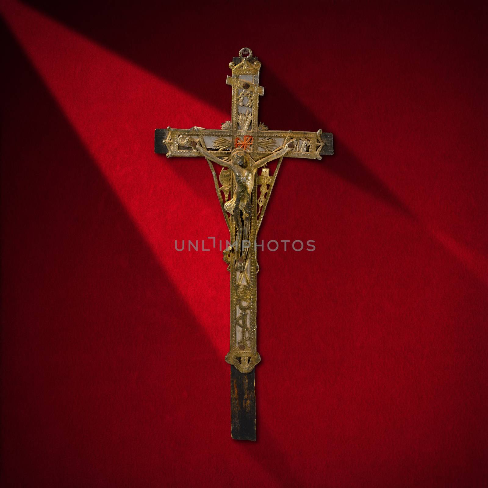 Ancient wooden cross with Jesus in silver on red velvet background with shadows